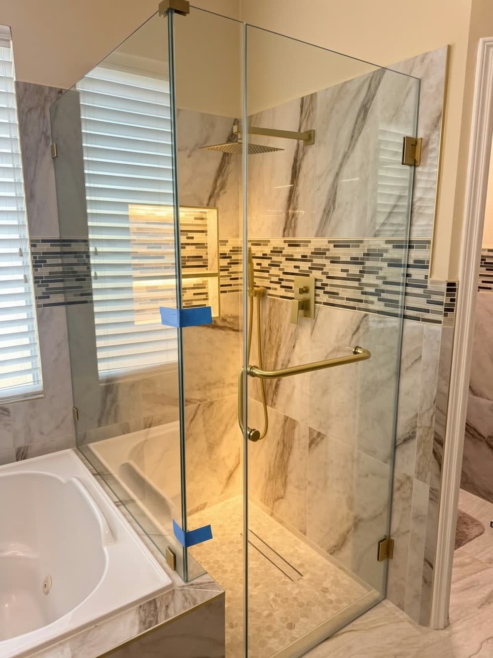 Corner glass shower with brushed-gold hardware, marble-look tile and a mosaic accent band