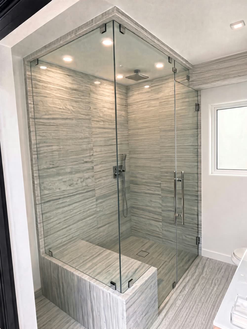 Frameless glass steam shower with gray linear stone-look tile and a built-in tiled bench — ProRock Remodeling, Bay Area