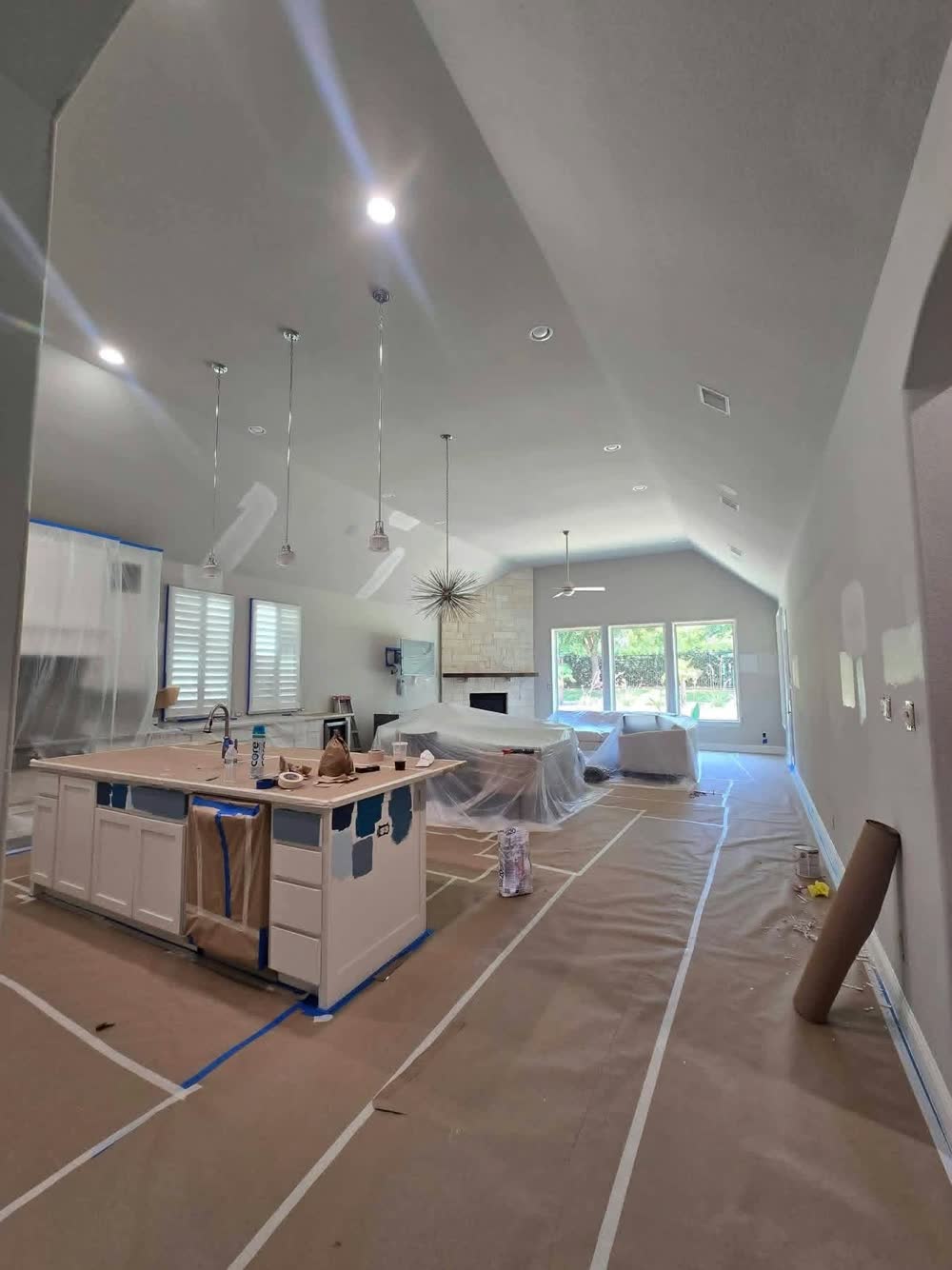 Kitchen installation in an open-plan room with a vaulted ceiling: white island and cabinets going in, floors covered for protection during a ProRock remodel