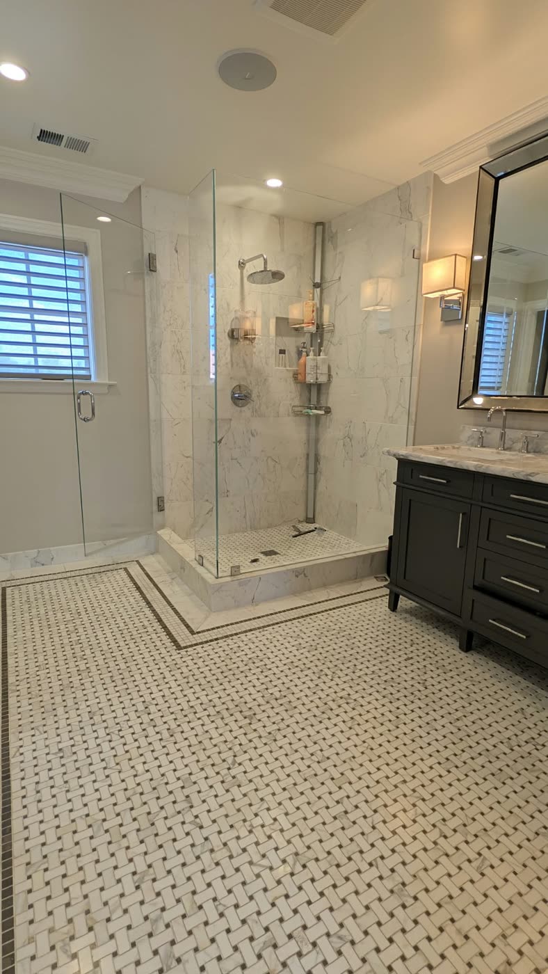 Primary bathroom with marble basketweave floor tile, a frameless glass shower and a dark vanity