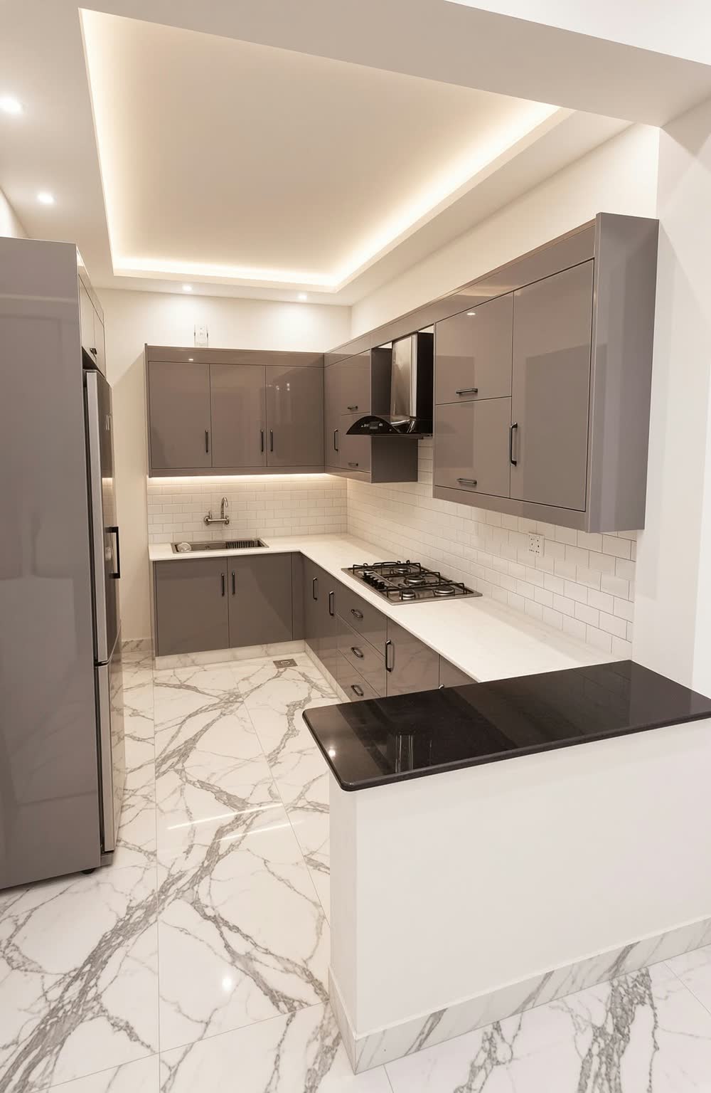 Modern U-shaped kitchen with glossy gray cabinets, black countertops, a lit tray ceiling and marble-look floors