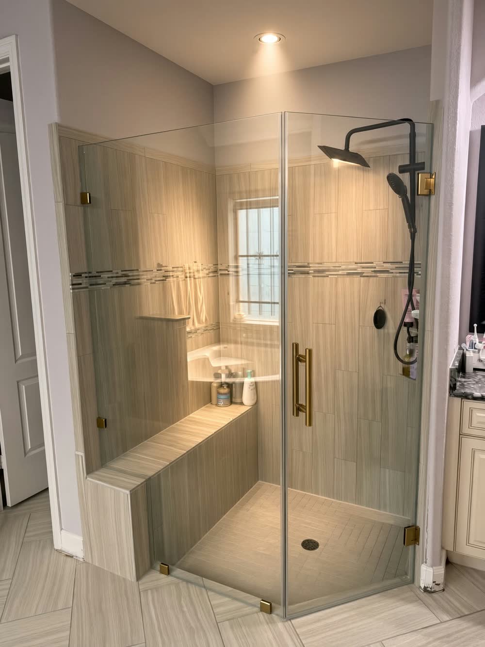 Neo-angle glass shower with a built-in bench, linear tile and gold and black fixtures — ProRock Remodeling, Bay Area