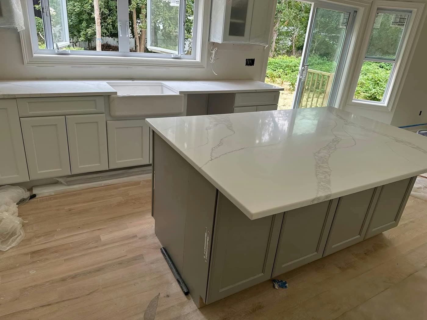 Kitchen with a white quartz island on gray shaker cabinets and a farmhouse sink under large windows — ProRock Remodeling, Bay Area