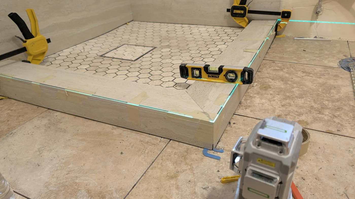 Shower curb checked with a laser level and spirit levels next to a hexagon mosaic shower floor