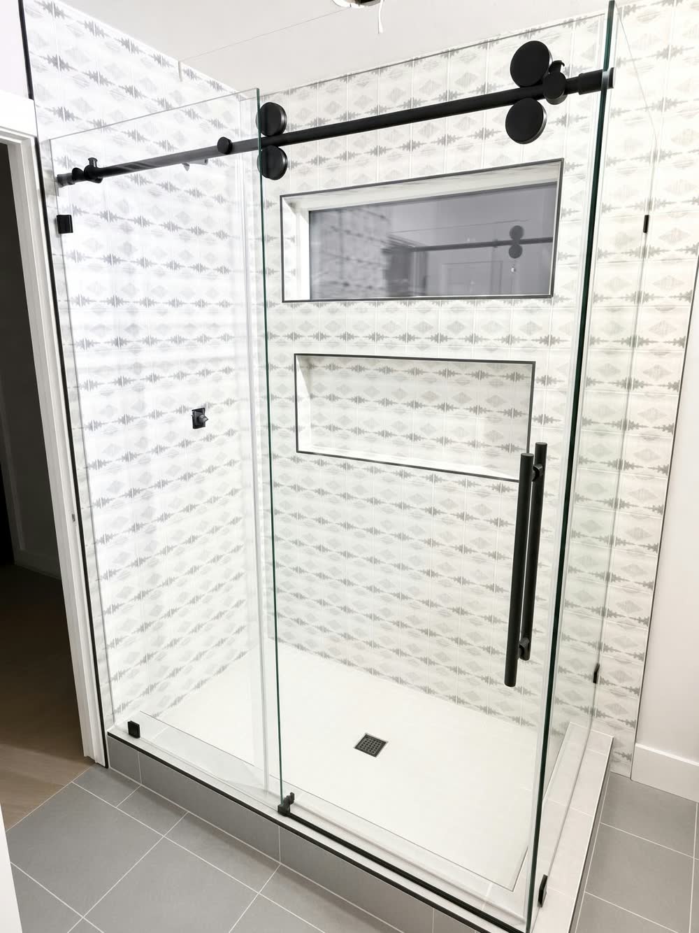 Sliding glass shower enclosure with matte black hardware, white textured wall tile and a long niche — ProRock Remodeling, Bay Area