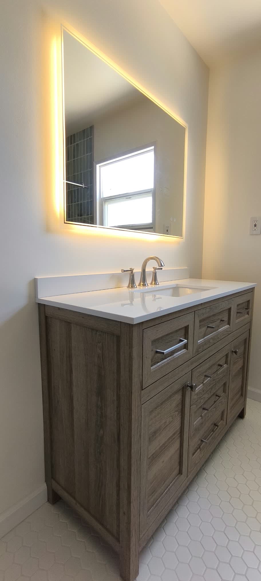 Gray wood bathroom vanity with a white top under a backlit LED mirror — ProRock Remodeling, Bay Area