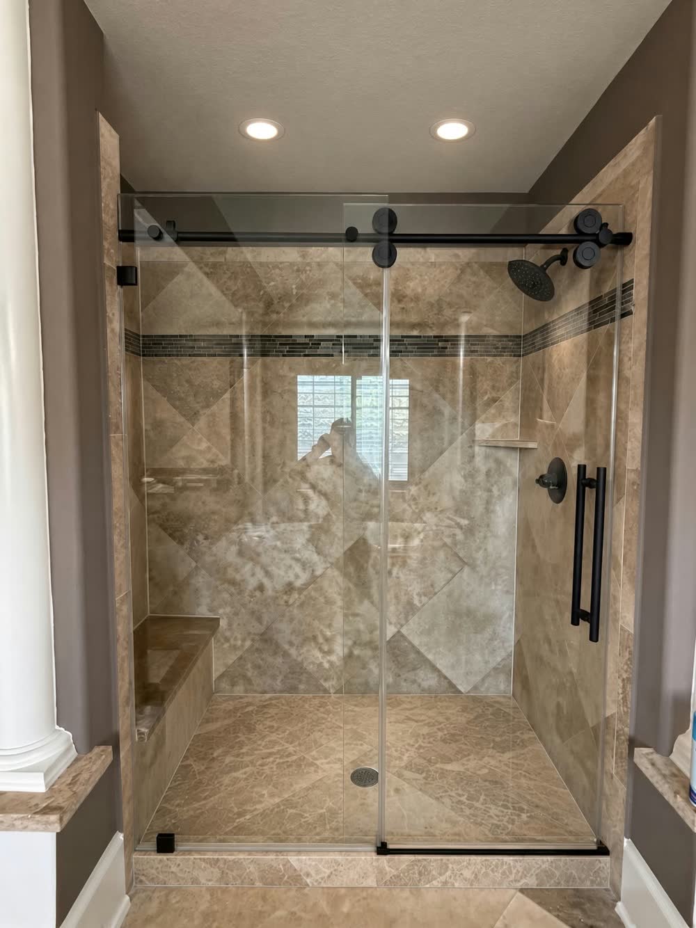 Walk-in shower with a built-in bench, travertine-look tile and a sliding glass door with black hardware — ProRock Remodeling, Bay Area