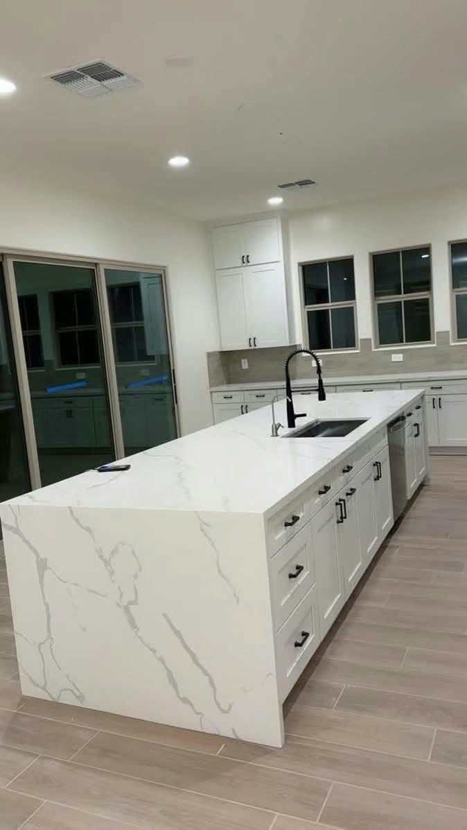 Long white kitchen island with a waterfall quartz edge and a black faucet