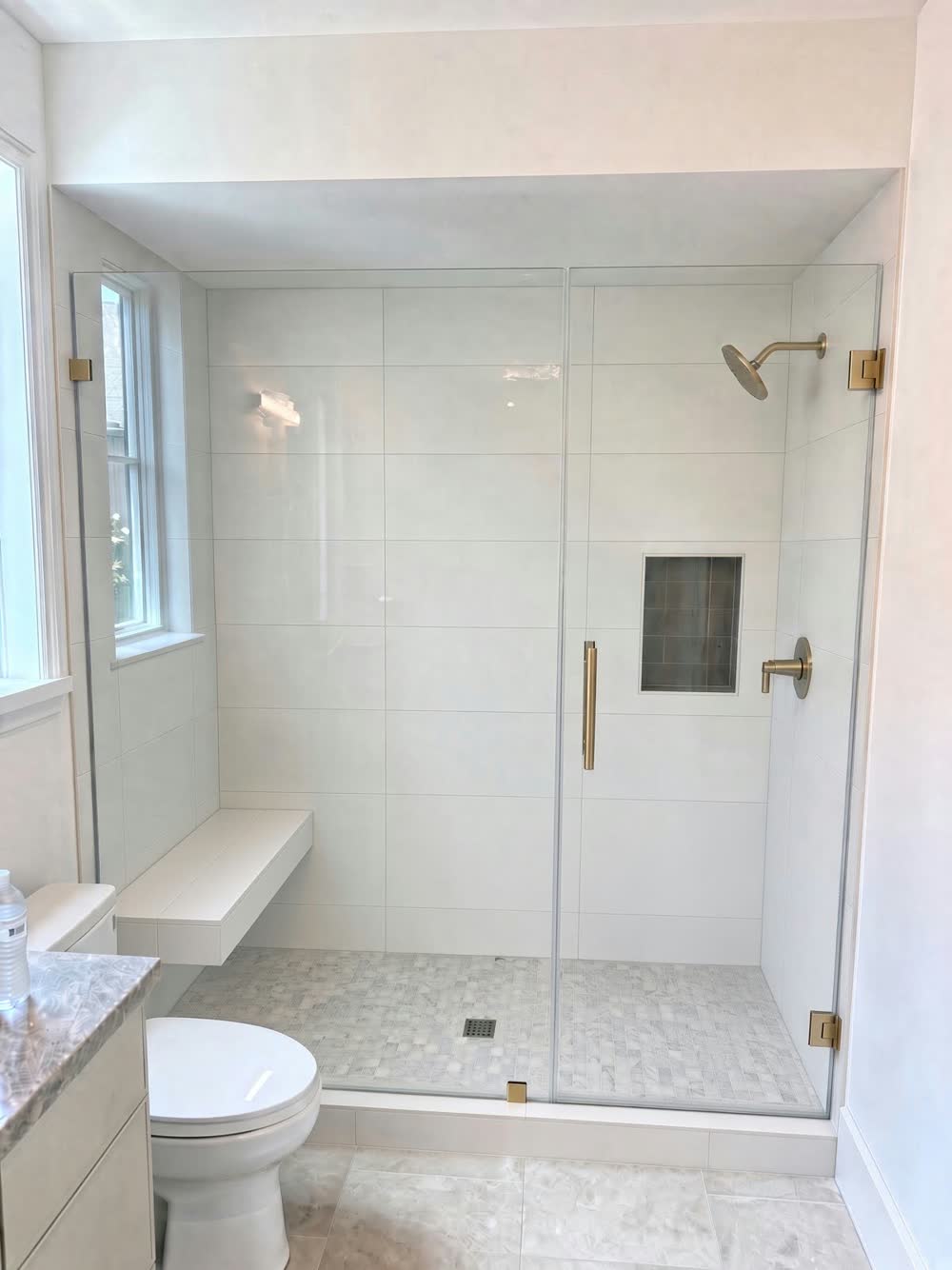 White walk-in shower with a frameless glass door, built-in bench, wall niche and brass fixtures — ProRock Remodeling, Bay Area